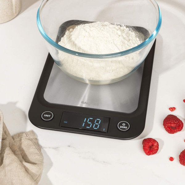 Glass bowl with milk being poured, on digital kitchen scale showing zero.