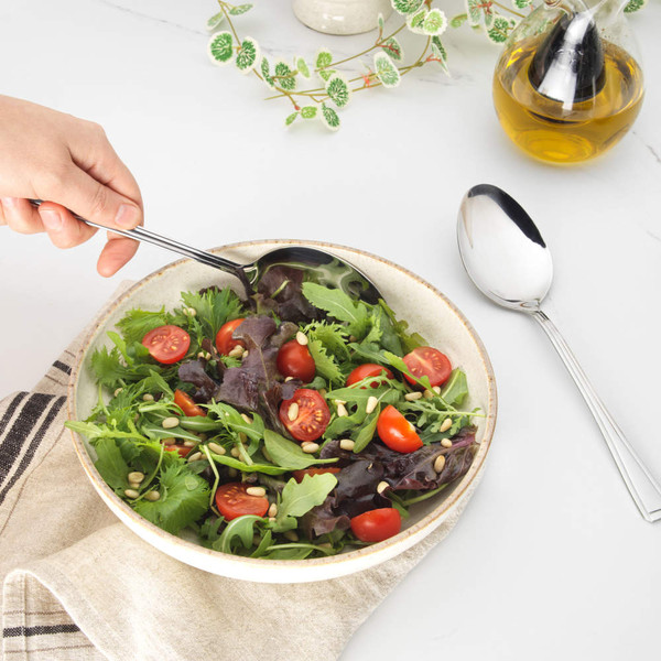 Set of two stainless steel serving spoons on woven placemat, tabletop setting