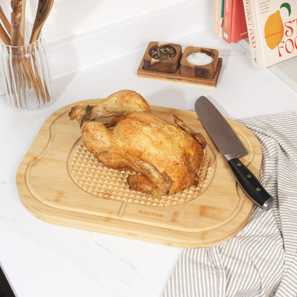 Roast chicken on bamboo carving board with chef’s knife, kitchen setting.