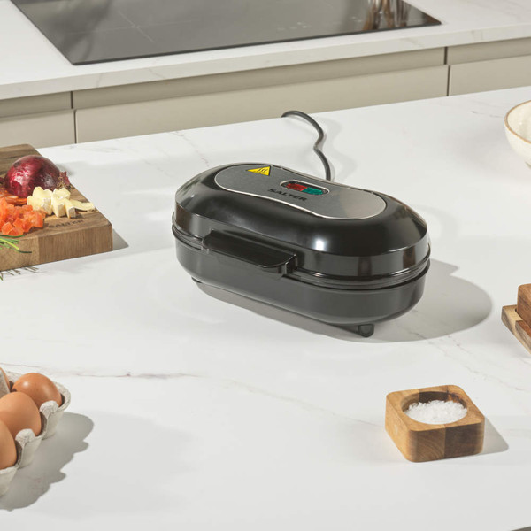 Electric breakfast sandwich maker with round non-stick plates and a cooked omelette being lifted out