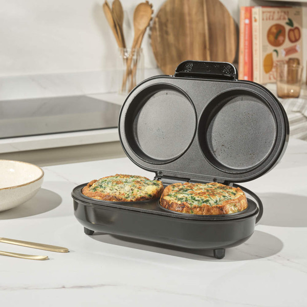 Black electric omelette maker open with two cooked omelettes inside, shown on kitchen counter