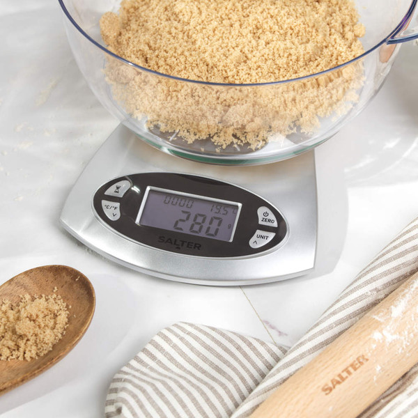 Digital kitchen scale weighing bowl of brown sugar for baking, shown on a countertop