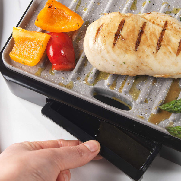 Grey electric grill surface with fat collection tray, close-up showing textured non-stick coating
