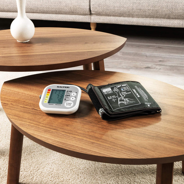 Digital upper arm blood pressure monitor with cuff on wooden coffee table