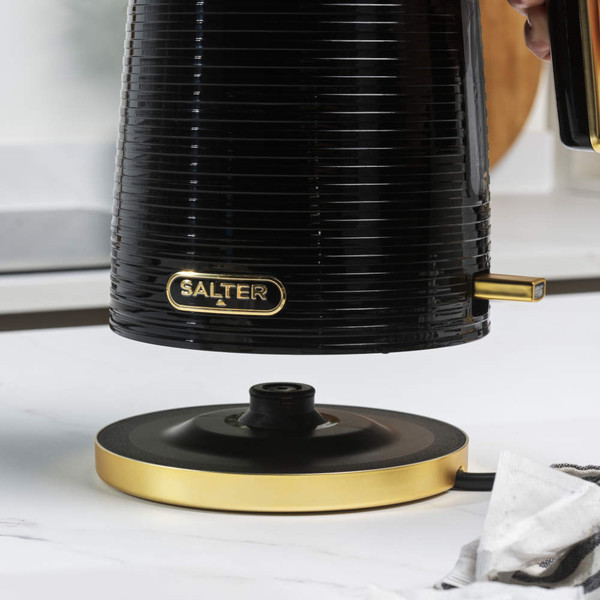 Black and gold Salter electric kettle with ridged finish, shown beside a cup of coffee.