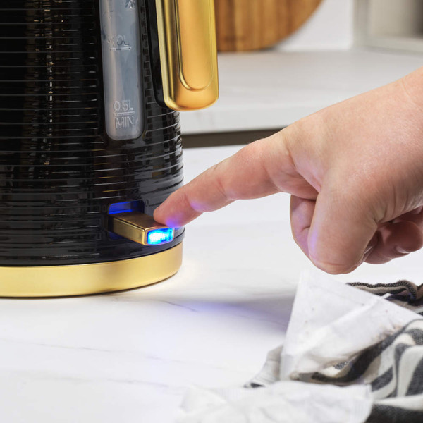 Hand turning on black and gold kettle with blue power light on kitchen worktop