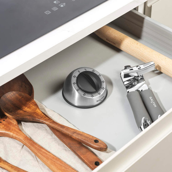 Silver kitchen timer with black dial on shelf next to wooden grinders, oven visible