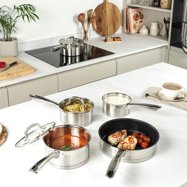Stainless steel saucepan with lid on wooden chopping board beside fresh tomatoes and knife