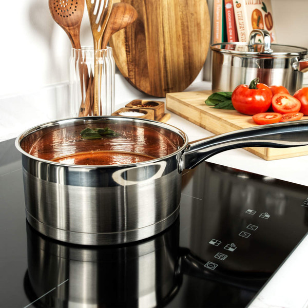Stainless steel saucepan with tomato sauce on induction hob, fresh tomatoes in background