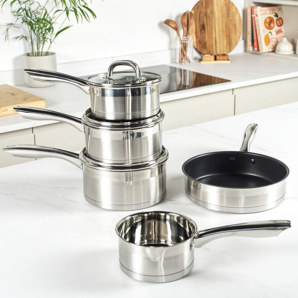 Set of stainless steel saucepans and frying pan on kitchen counter, food shown inside