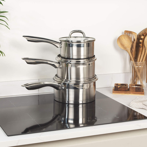 Set of three stainless steel saucepans with lids on induction hob