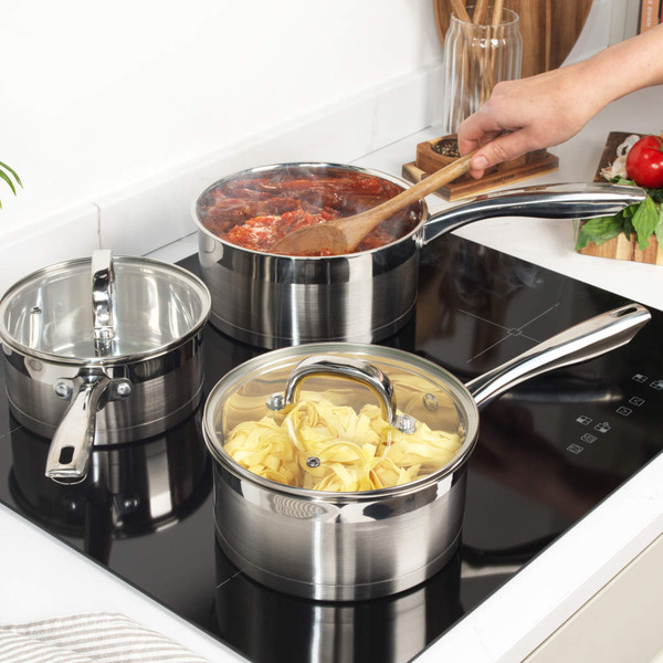 Set of three silver stainless steel saucepans with glass lids on a kitchen worktop
