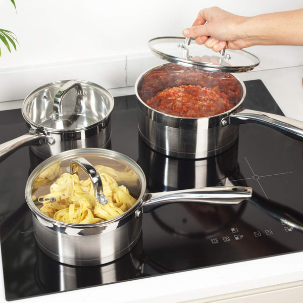 Set of three stainless steel saucepans with glass lids on an induction hob, in use.