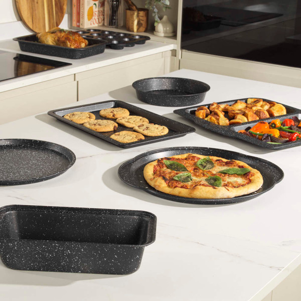 Set of grey speckled non-stick bakeware displayed with pizza, cookies, and roast vegetables