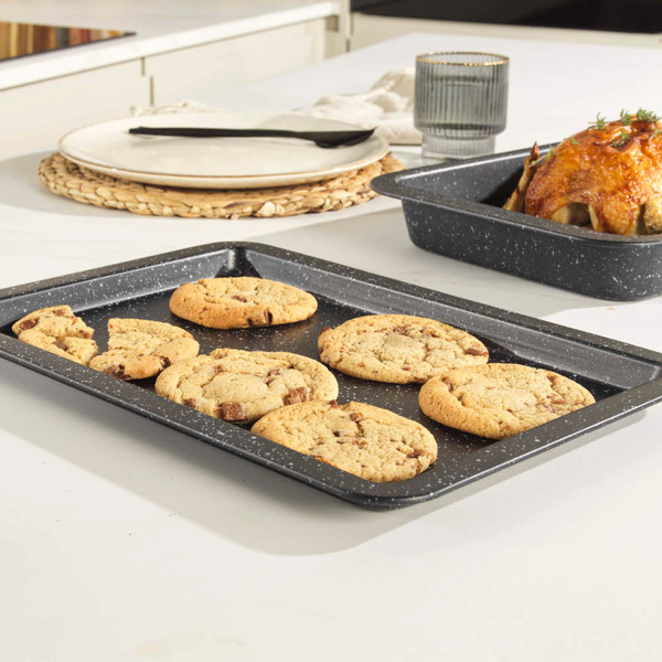 Non-stick grey baking tray with six chocolate chip cookies on kitchen worktop