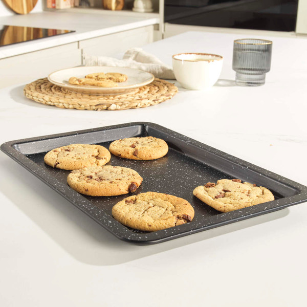 Non-stick baking tray with five chocolate chip cookies, shown on a kitchen worktop.