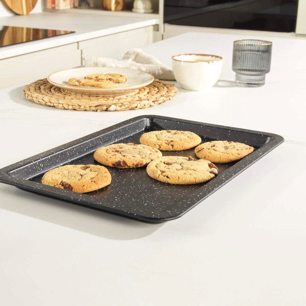 Grey non-stick baking tray with five chocolate chip cookies, shown in a modern kitchen.