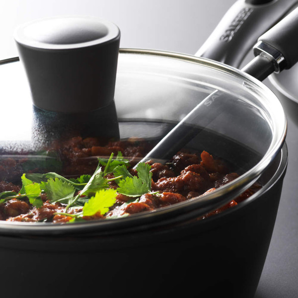 Black non-stick saucepan with glass lid, showing cooked stew garnished with coriander