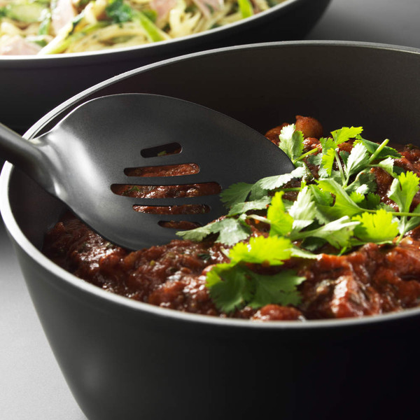 Black nylon slotted serving spoon in non-stick saucepan with tomato-based stew, topped with coriander