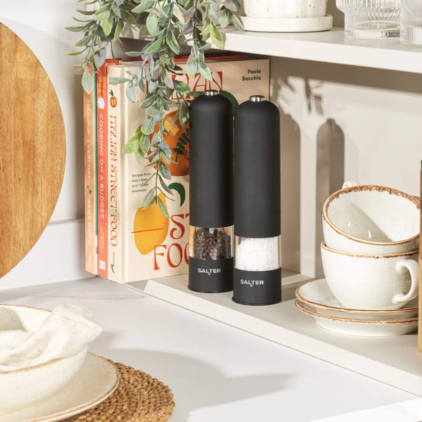 Hand measuring salt over electric grinder in modern kitchen setting