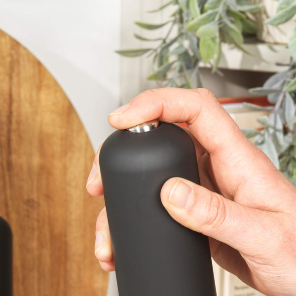 Black matte salt or pepper grinder in hand, shown from side with button on top