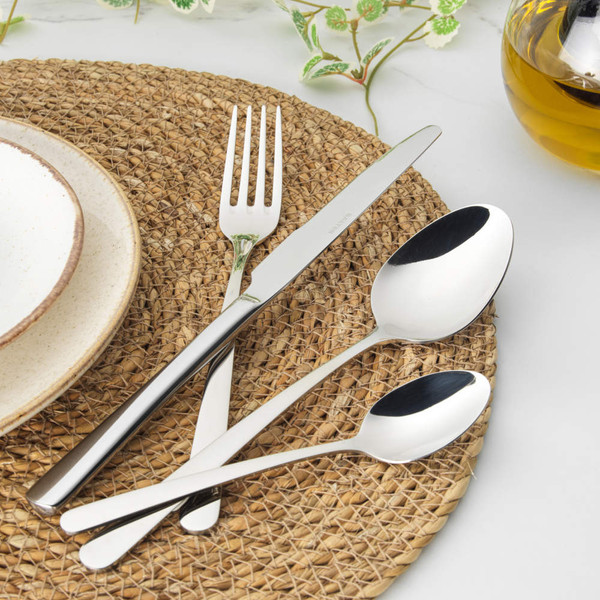 Hand holding silver fork with cake slice on plate, stoneware mug and cutlery nearby