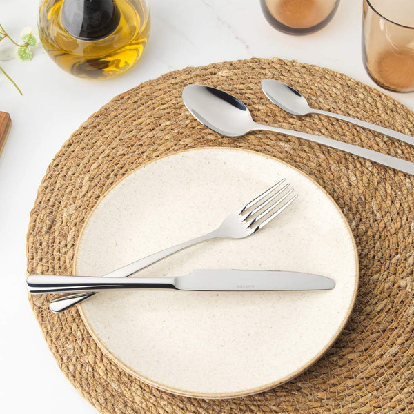 Neutral ceramic dinner plate on woven placemat with cutlery, coffee cup, and olive oil bottle