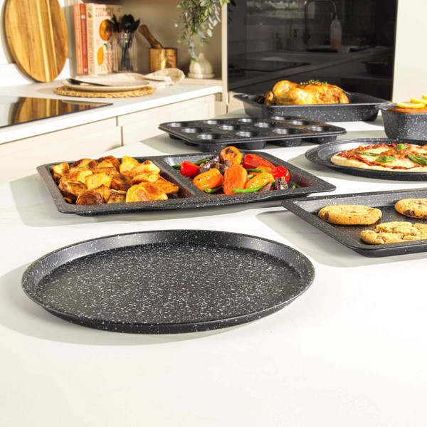 Set of black speckled non-stick bakeware shown with roast, pizza, cookies and veg.