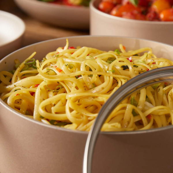 Cooked linguine pasta with chopped herbs and peppers in a beige bowl, lid to one side