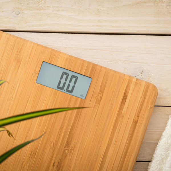 Digital bamboo bathroom scale with LCD display, shown on wooden floor beside white towel.