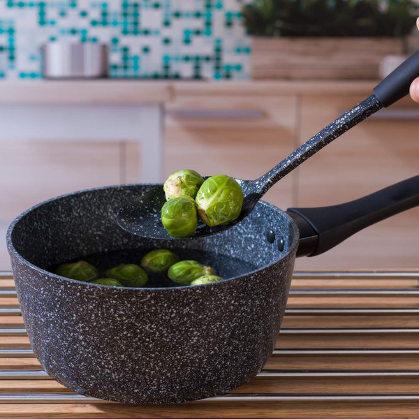 Black speckled saucepan with brussels sprouts on slotted spoon in kitchen