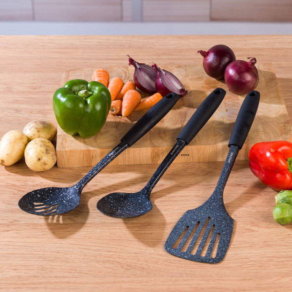 Set of three black-handled kitchen utensils on wooden table with fresh vegetables.