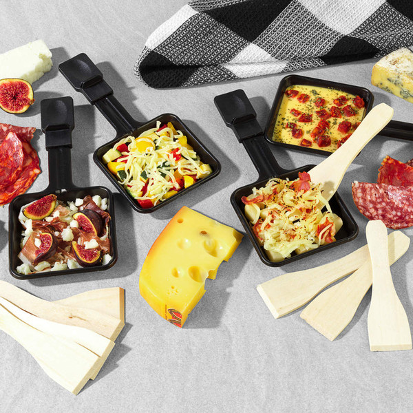 Raclette pans with mixed toppings, cheese and cured meats for tabletop serving.