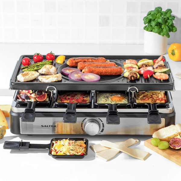 Tabletop electric raclette grill with fondue pot and food, shown in kitchen setting