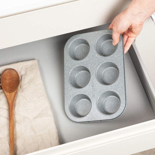 Grey six-cup muffin tray with speckled finish, shown being placed in kitchen drawer