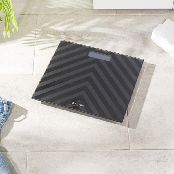 Black glass bathroom scale with striped pattern, shown on tiled floor