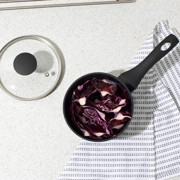 Black saucepan with purple cabbage on white worktop, lid and tea towel beside