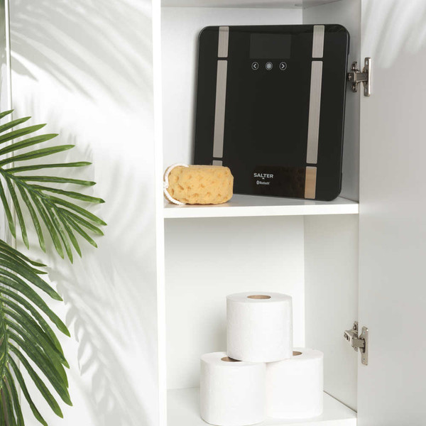 Black digital bathroom scale with silver accents on shelf beside bath sponge
