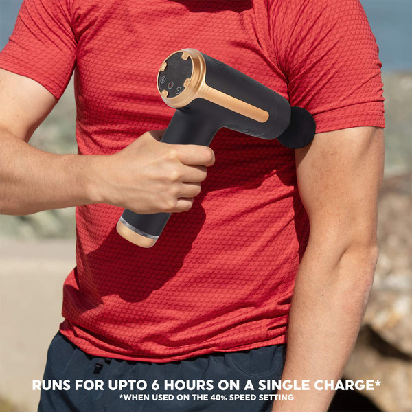 Black and gold massage gun used on upper arm, outdoors.