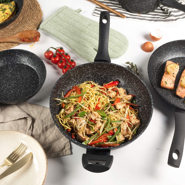 Black marble-effect wok pan with stir fry noodles, chicken, and vegetables on kitchen counter.