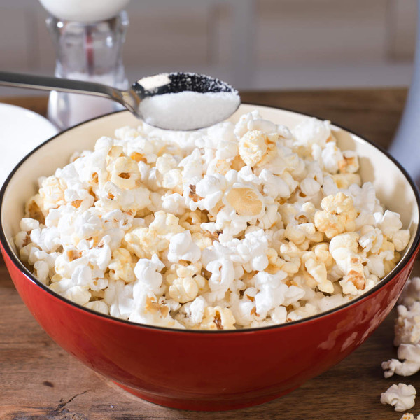 Large bowl of plain popcorn with a spoonful of sugar being added