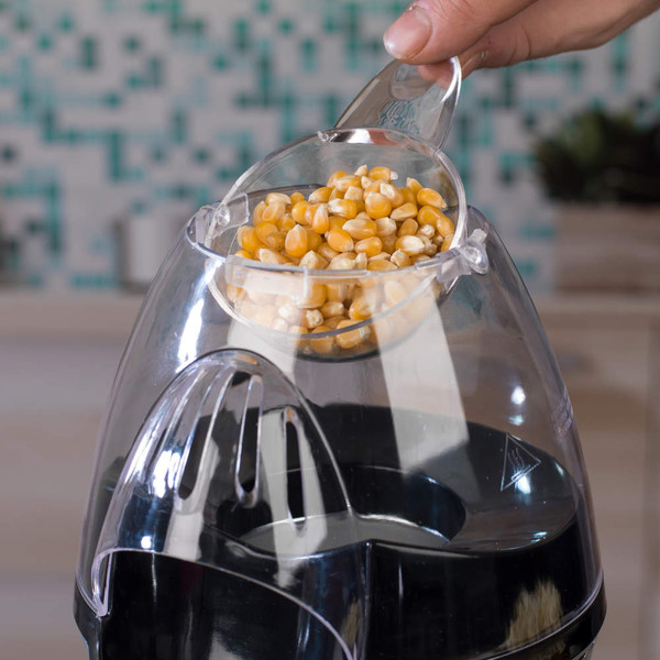 Hand pouring popcorn kernels into a clear electric popcorn maker