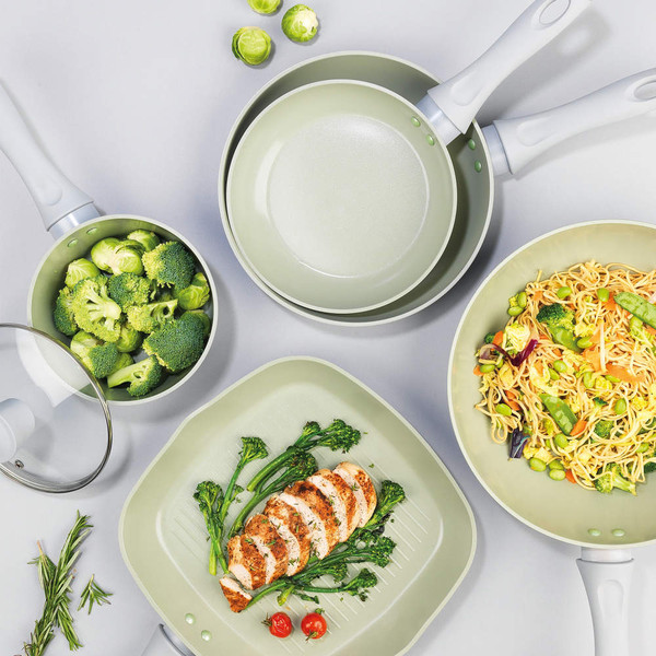 Set of light green non-stick saucepans and frying pan with prepared food, top-down view