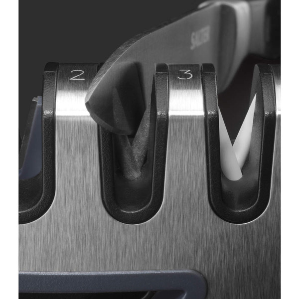 Close-up of knife blade in a multi-stage metal knife sharpener, showing sharpening slots.