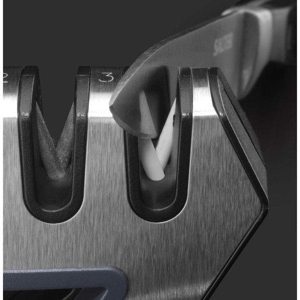 Close-up of knife blade being sharpened in manual knife sharpener, stainless steel finish.