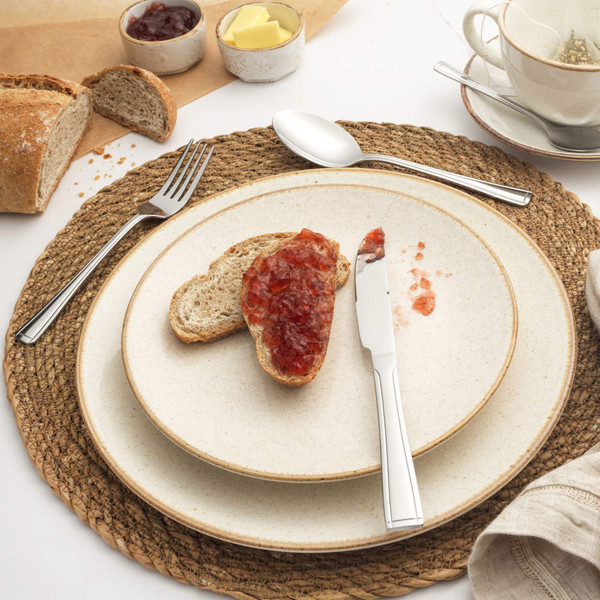 Slice of wholemeal bread with strawberry jam on plate, with butter and tea.