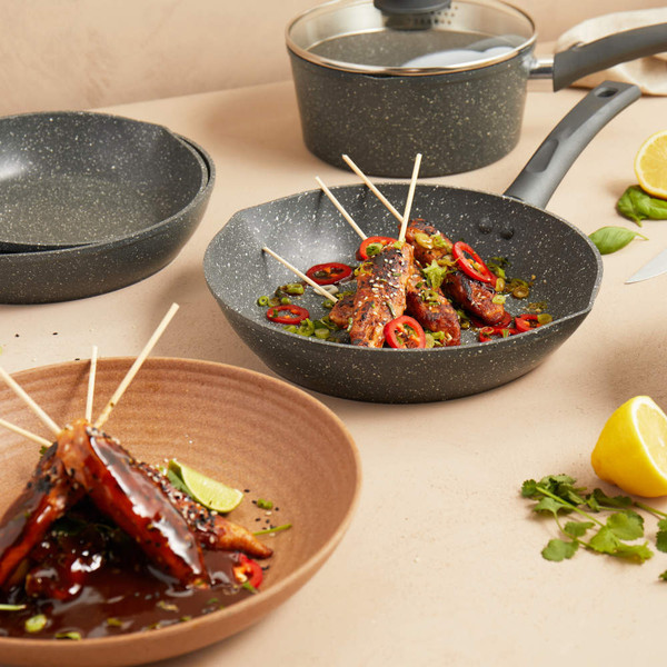 Grey non-stick saucepan and frying pan set shown with cooked skewers, kitchen setting