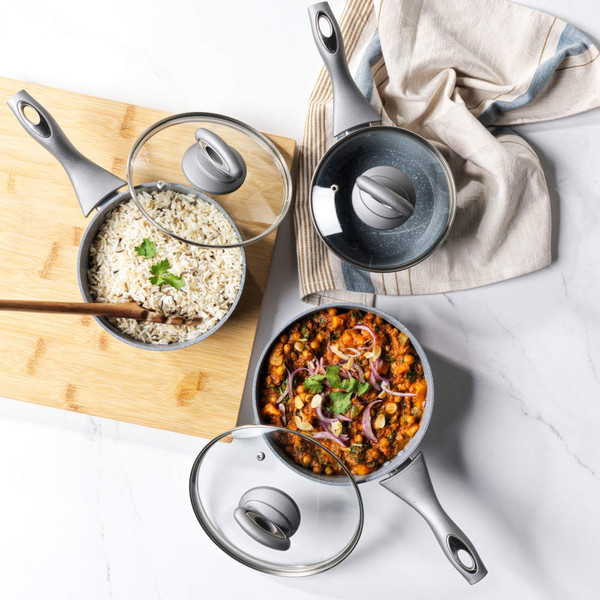 Set of three grey non-stick frying pans with glass lids, stacked side view