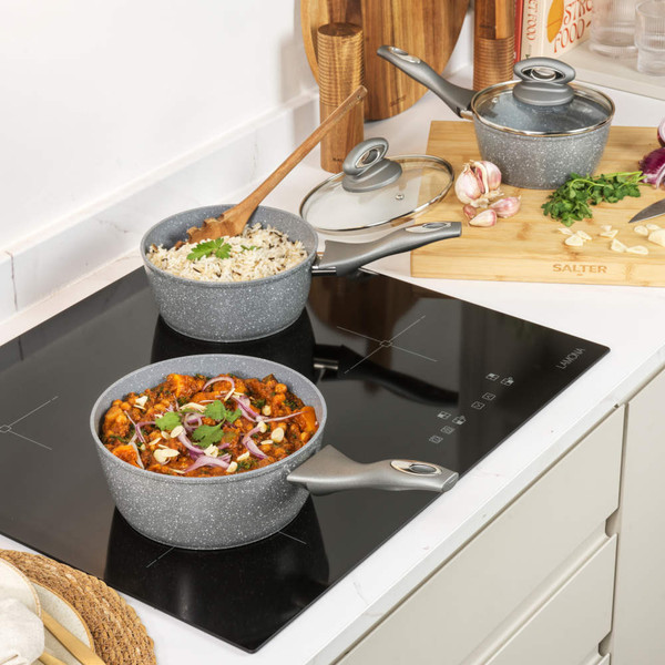 Set of grey non-stick pans and cookware with food, shown on a kitchen surface