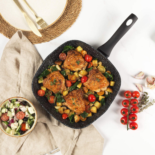 Square frying pan with cooked chicken thighs, potatoes and cherry tomatoes, top-down view